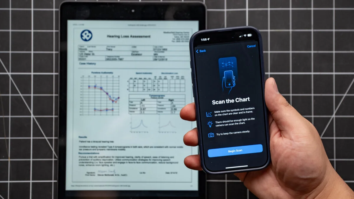 iPhone in hand showing manual process for adding hearing test data to phone. iPad in background showing audiogram.