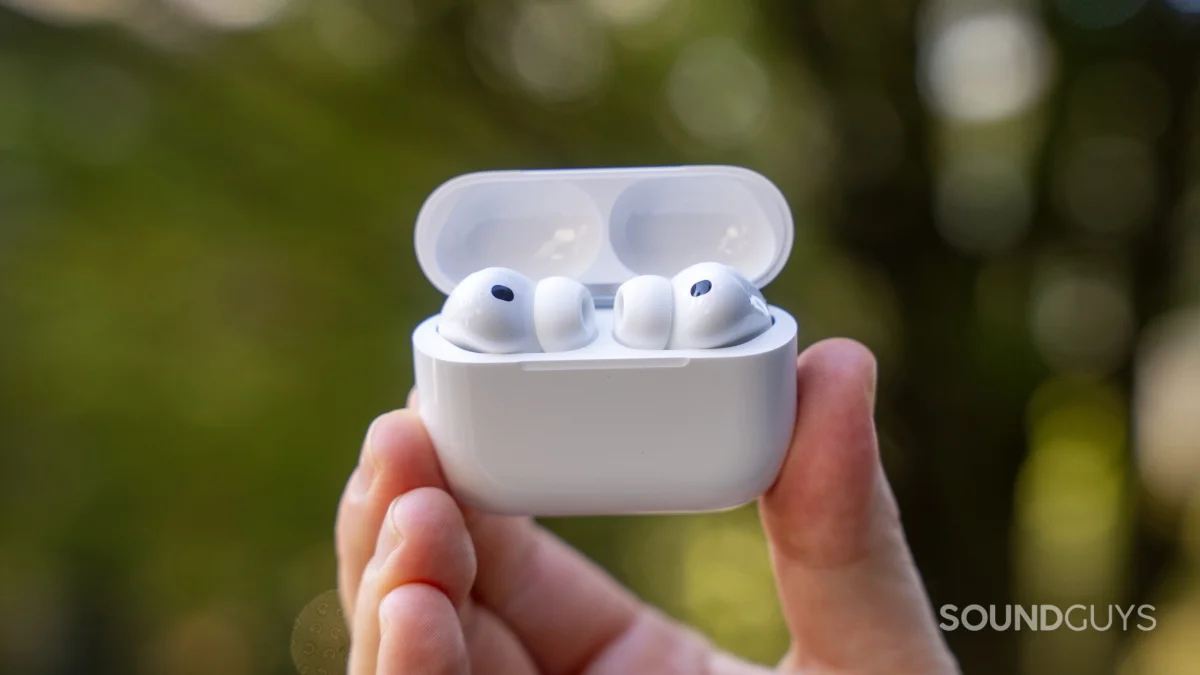 AirPods Pro 3 in hand outside in front of a bush.