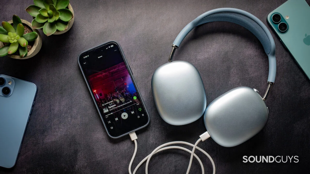 Apple AirPods Max 2 headphones on a table plugged into an iPhone 17 Pro playing music on Spotify.