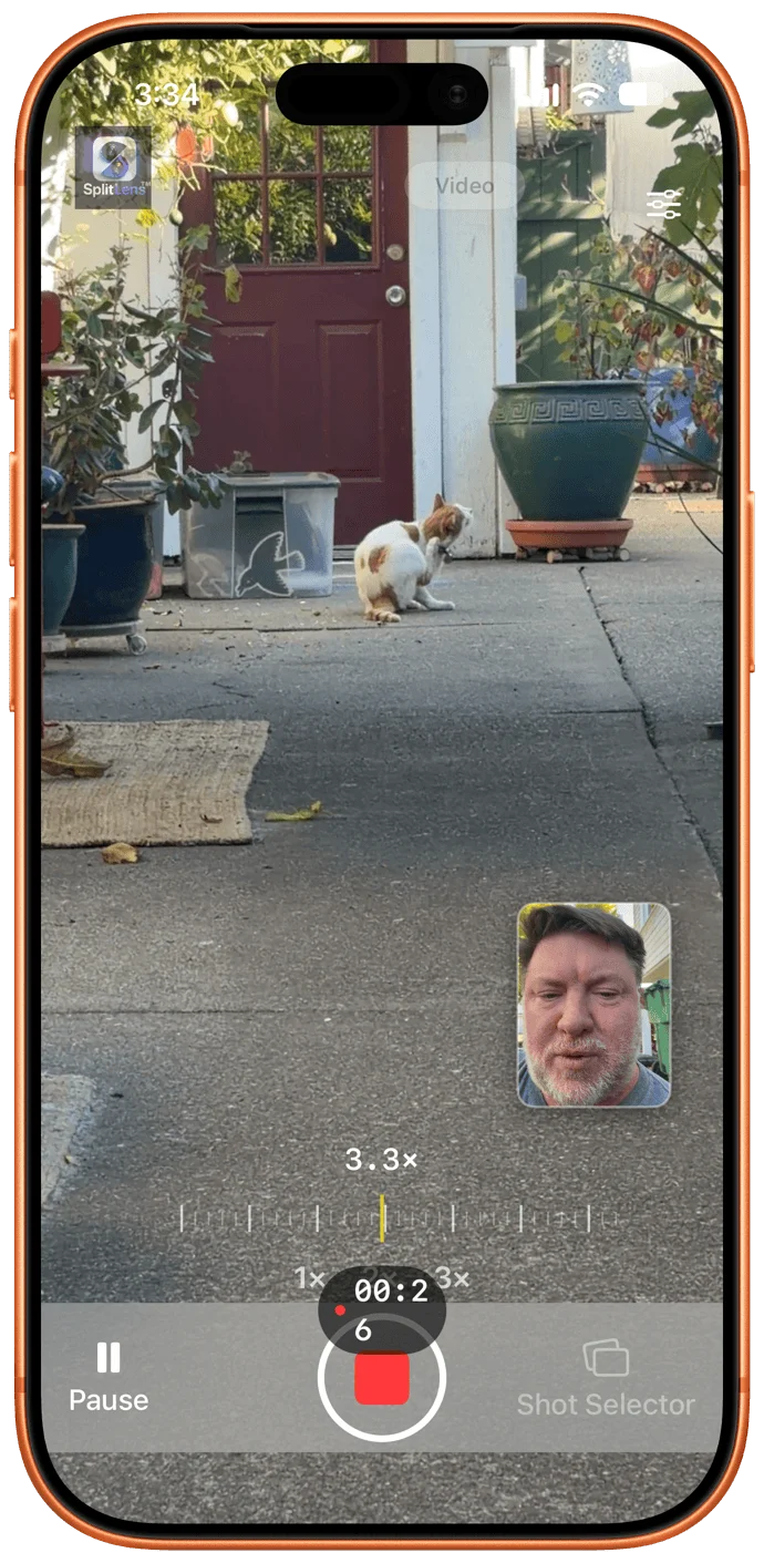 iPhone screenshot of the SplitLens camera app recording video at 3.3x zoom, 00:26 elapsed. A cat scratches itself in a courtyard by a red door. A small inset shows a bearded man on the front camera. Pause and Shot Selector buttons appear.