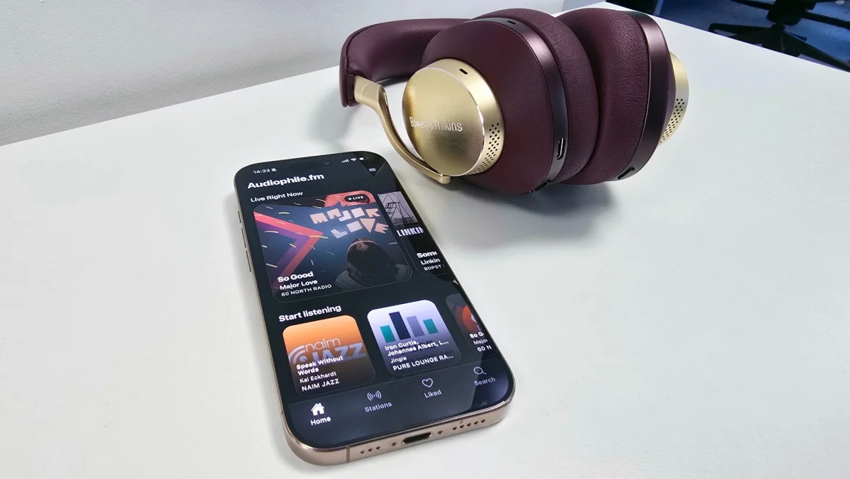 An iPhone with Audiophile.fm app on the screen, next to a pair of high-end Bowers & Wilkins headphones
